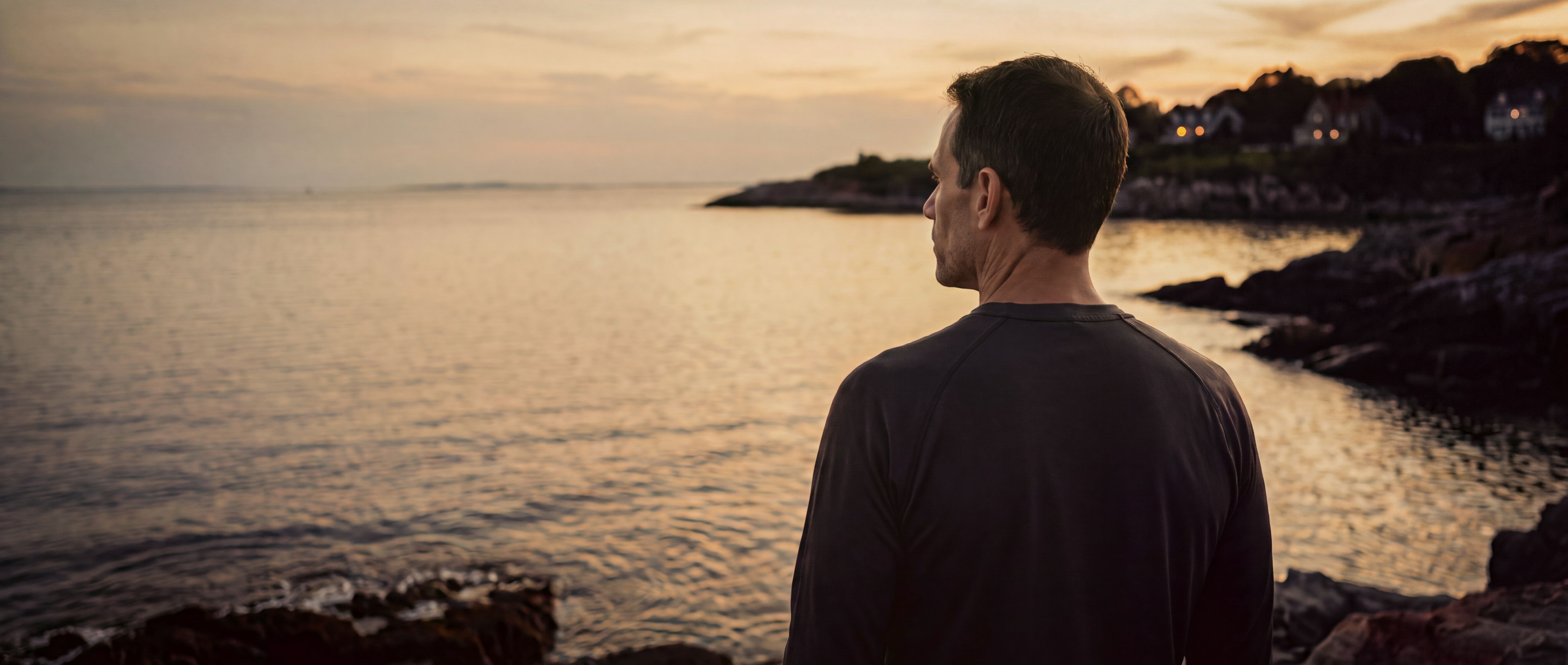 Franco Zuccoli seen from behind at dusk, looking out over the Atlantic from the Marblehead shore